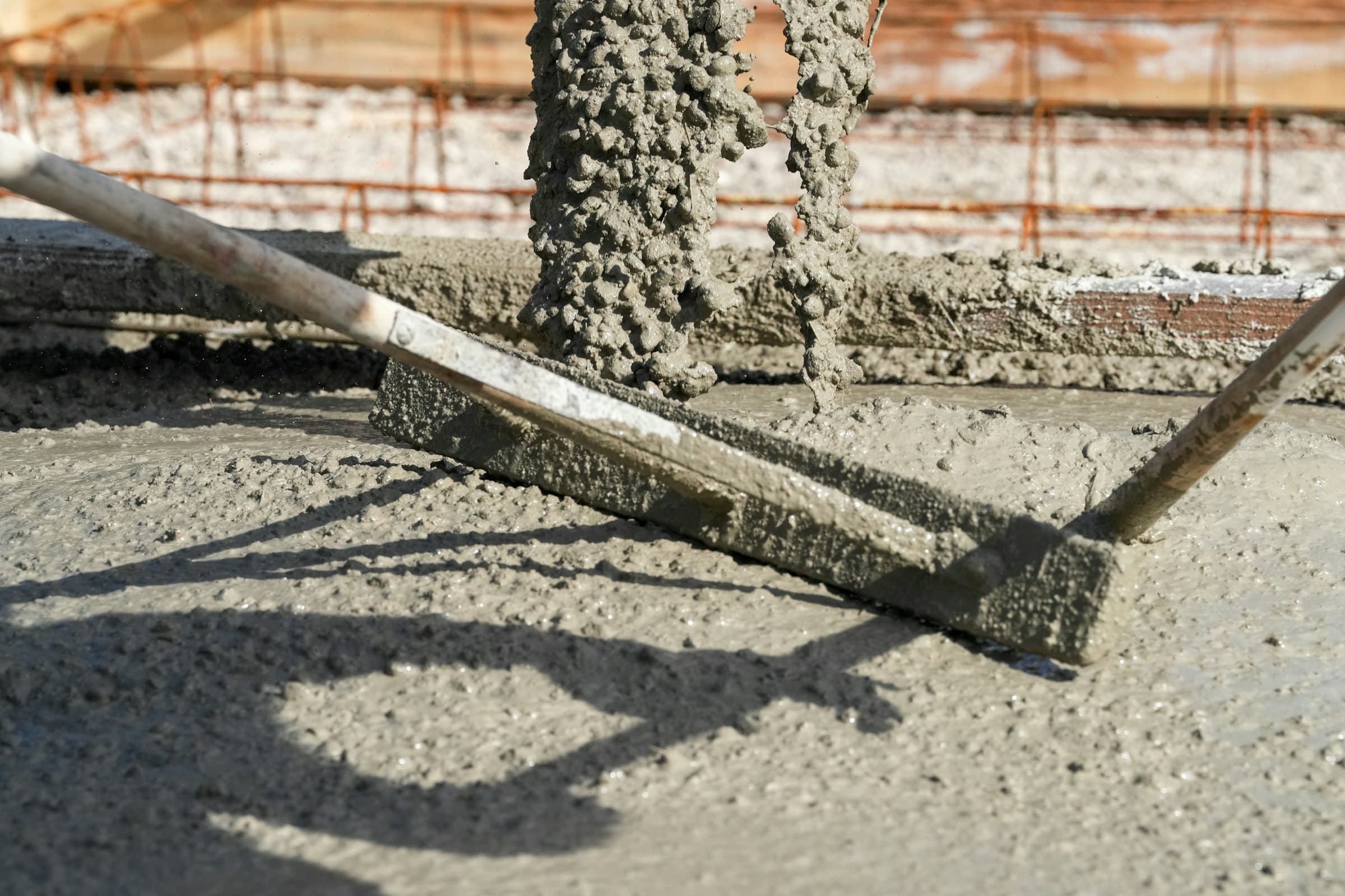 Worker levelling a liquid screed pour with a long screed bar